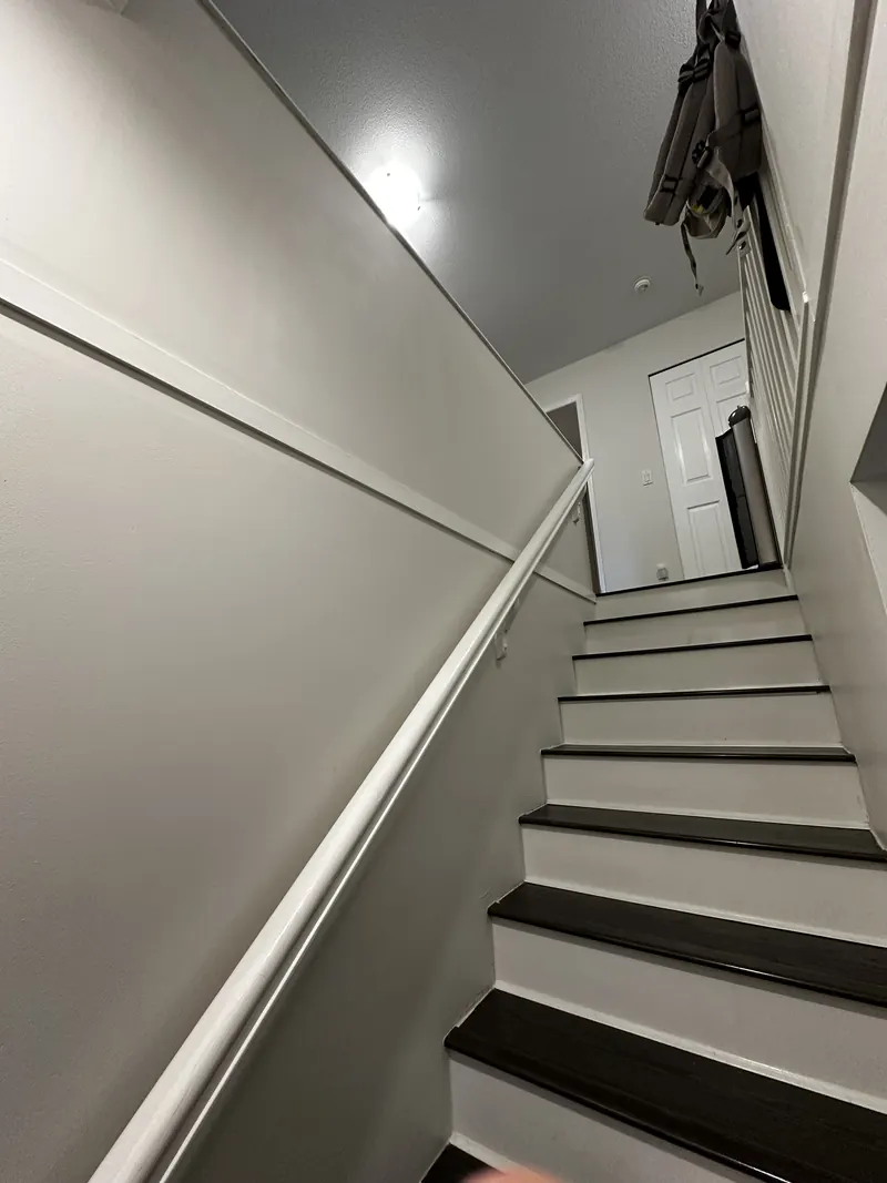 Stairwell with a painted skirt board, dark treads and a wall-mounted handrail