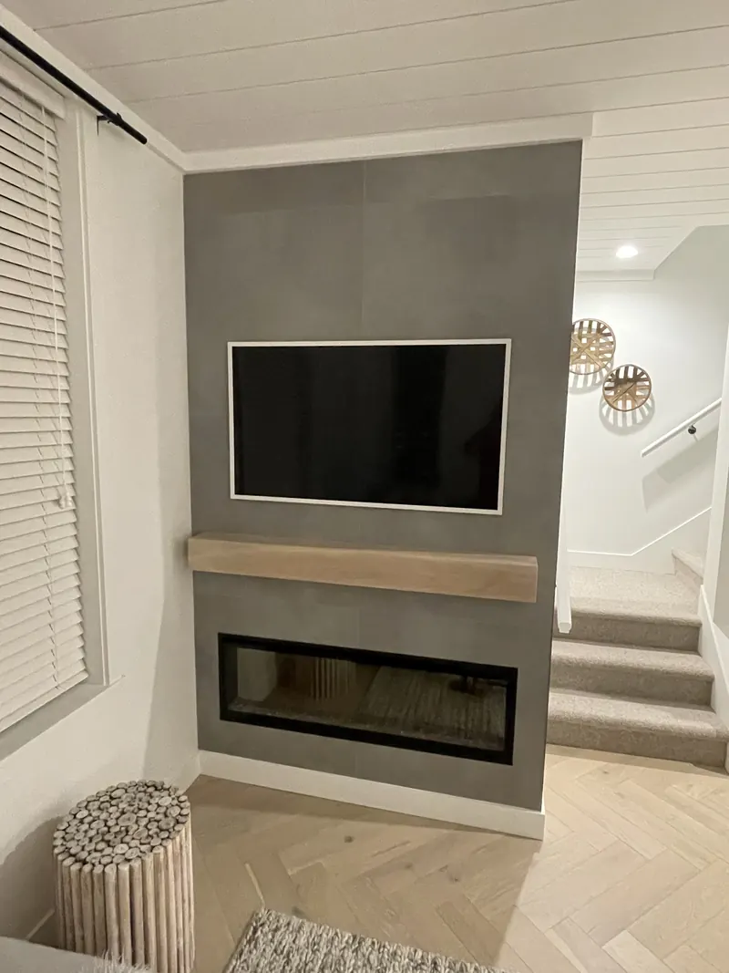 Linear electric fireplace in a concrete-finish feature wall with a floating oak mantel