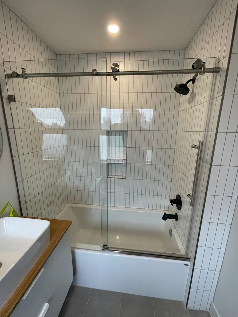 Vertical white tile tub surround with a sliding glass door and recessed niche